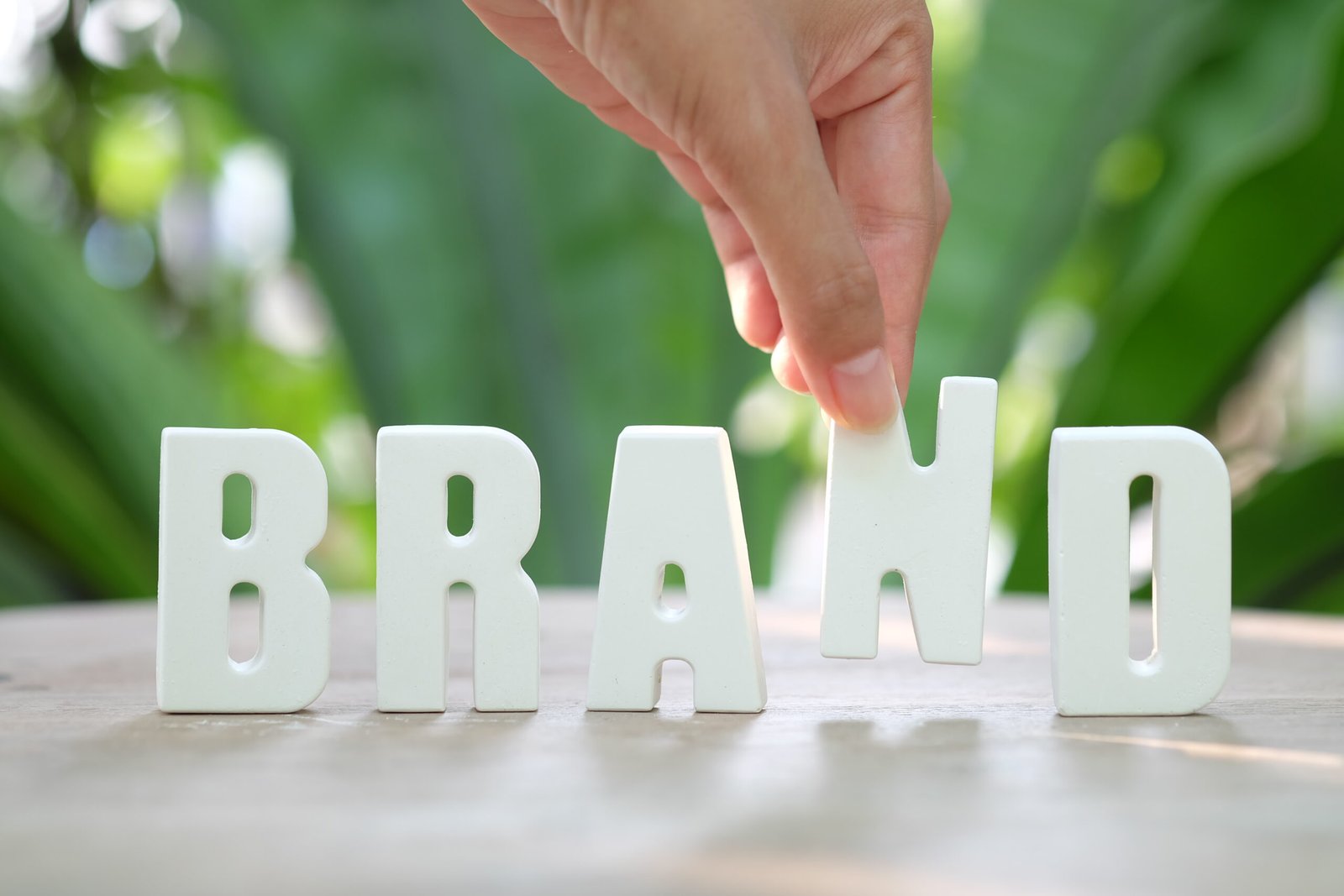 Hand arranging white letter tiles spelling BRAND